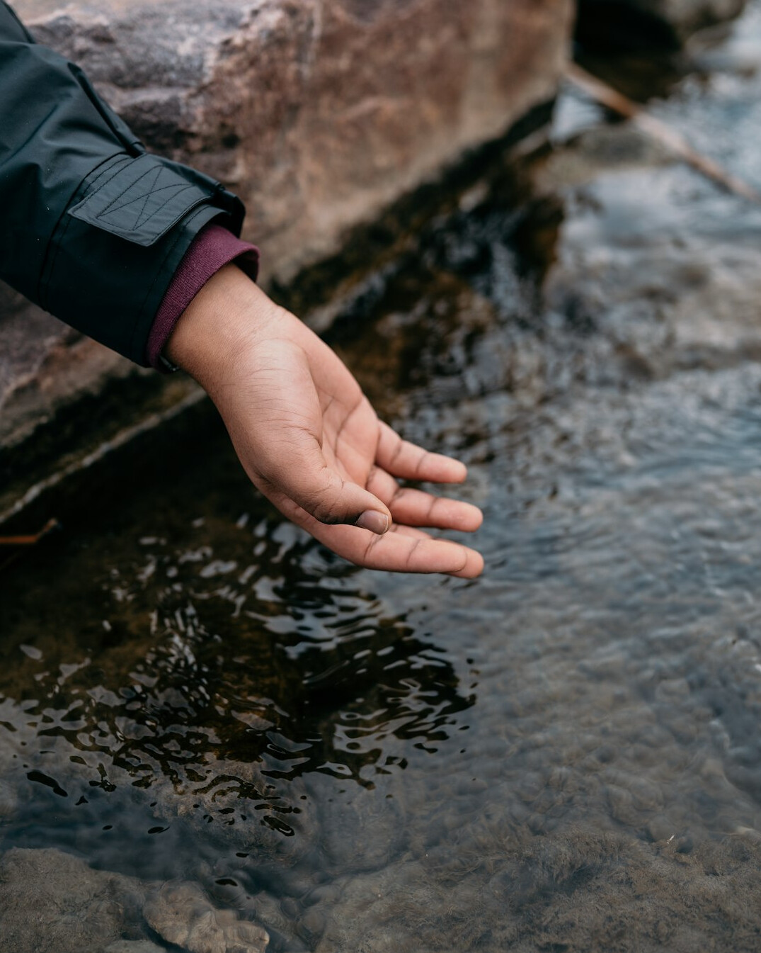 Hand collecting a water sample from a river for testing